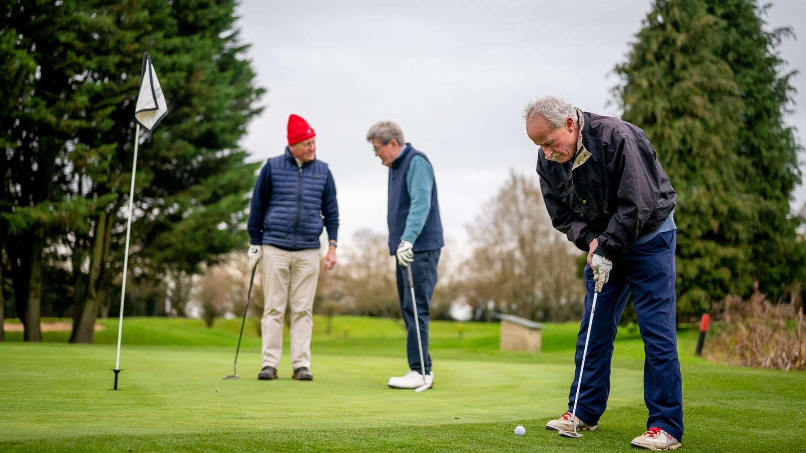 Tre voksne som spiller golf sammen